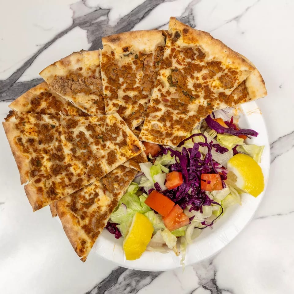 Lahmacun, a Turkish flatbread topped with minced meat, served with a fresh salad and lemon wedges.