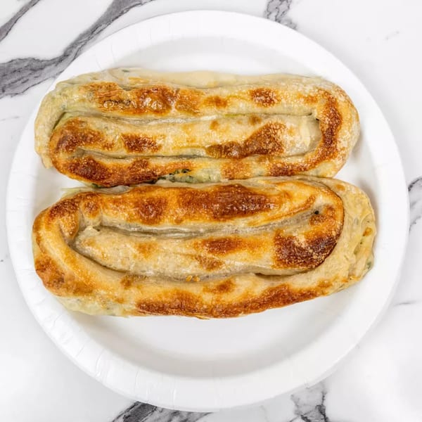 Two golden-brown, spiral-shaped pastries, possibly burek, on a white paper plate against a marble background.