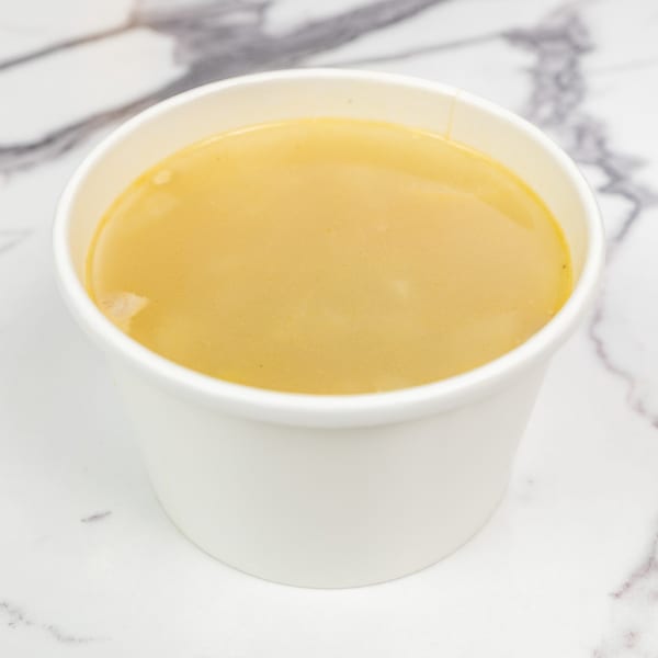Creamy yellow soup in a white paper cup on a white marble surface.