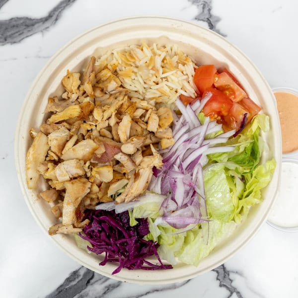 A chicken shawarma bowl with rice, lettuce, tomatoes, red onions, and purple cabbage.