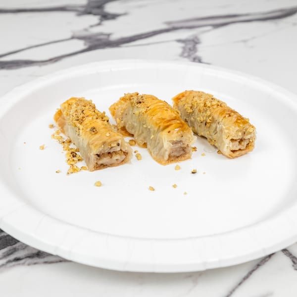 Three golden-brown baklava rolls, topped with chopped nuts, on a white paper plate.
